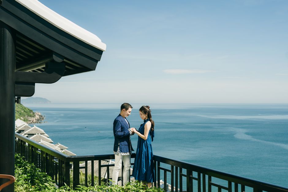 An elegant couple stands on the balcony of their modern Los Cabos property, looking out at a beautiful ocean sunset, representing a successful real estate purchase.