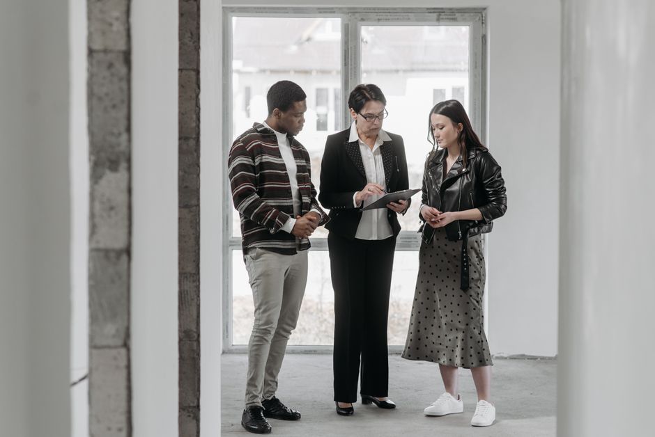 A professional and friendly real estate agent showing a well-dressed couple documents on a tablet inside a bright, modern luxury home with large windows.