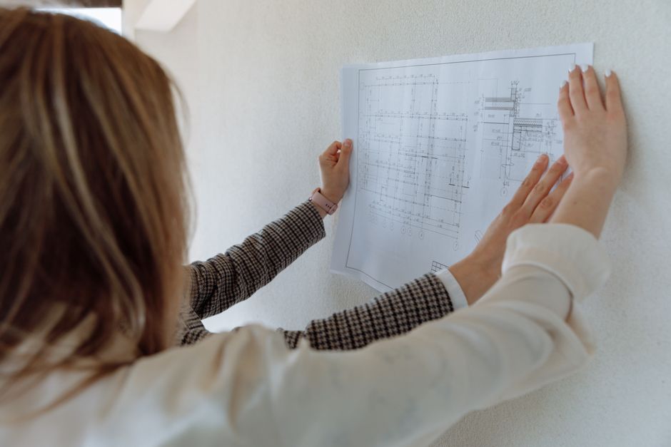 Professional fiduciary stands in front of a home, looking thoughtfully at a set of blueprints, representing the careful de...